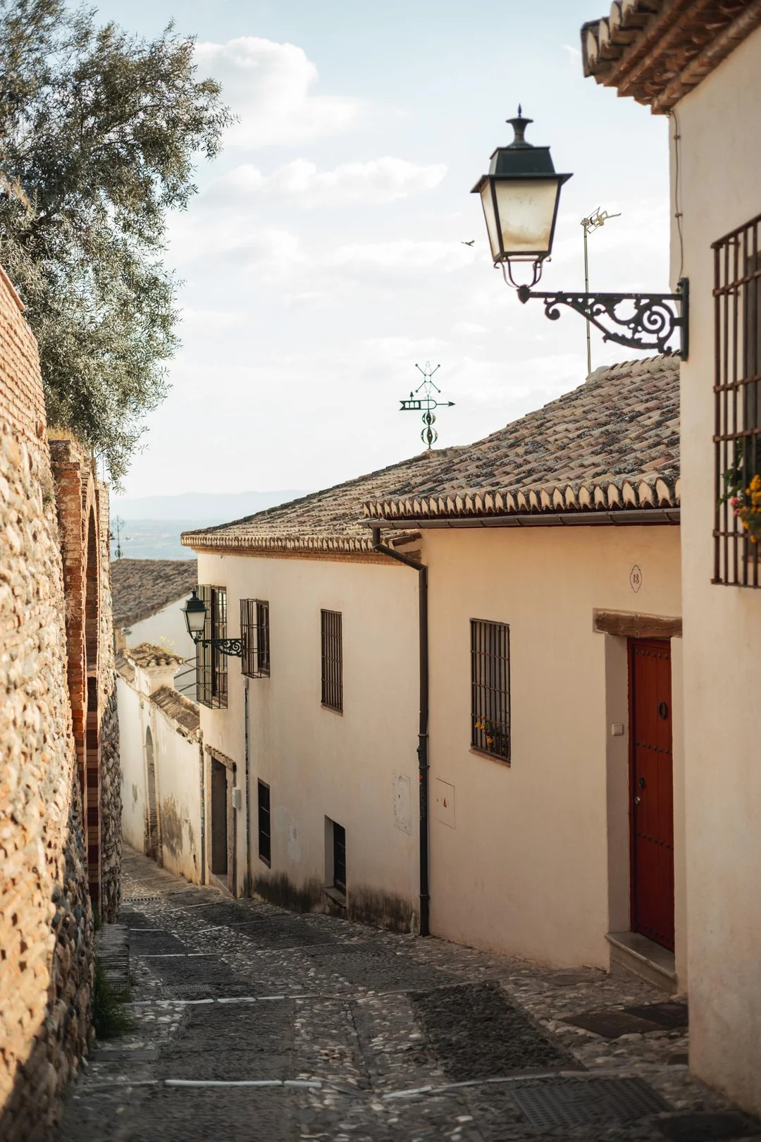 A narrow cobblestone street with whitewashed houses and vintage lanterns in the historic Albaicín district of Granada, showcasing timeless historical Andalusian architecture captured by Zihman Photo.
